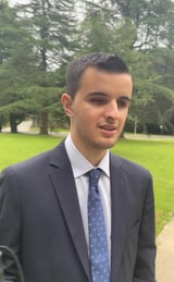 Iván Novegil, un hombre joven con traje oscuro y corbata azul, fotografiado al aire libre en un parque con césped y árboles al fondo