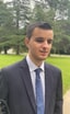 Iván Novegil, un hombre joven con traje oscuro y corbata azul, fotografiado al aire libre en un parque con césped y árboles al fondo