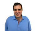 Agustín Aguirre, sonriendo y vestido con un polo azul, fotografiado de frente sobre un fondo blanco
